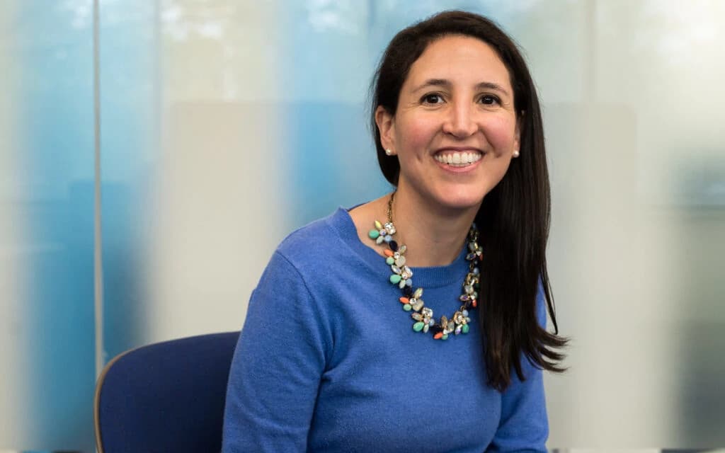Portrait of Cristina, a professional woman with glasses smiling confidently in a bright office setting