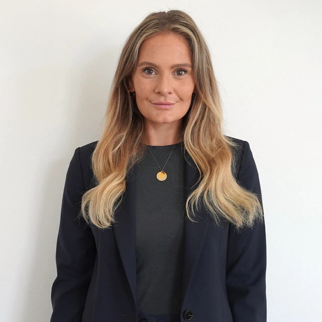 Professional woman wearing a black blazer and white blouse standing confidently with arms crossed against a plain background