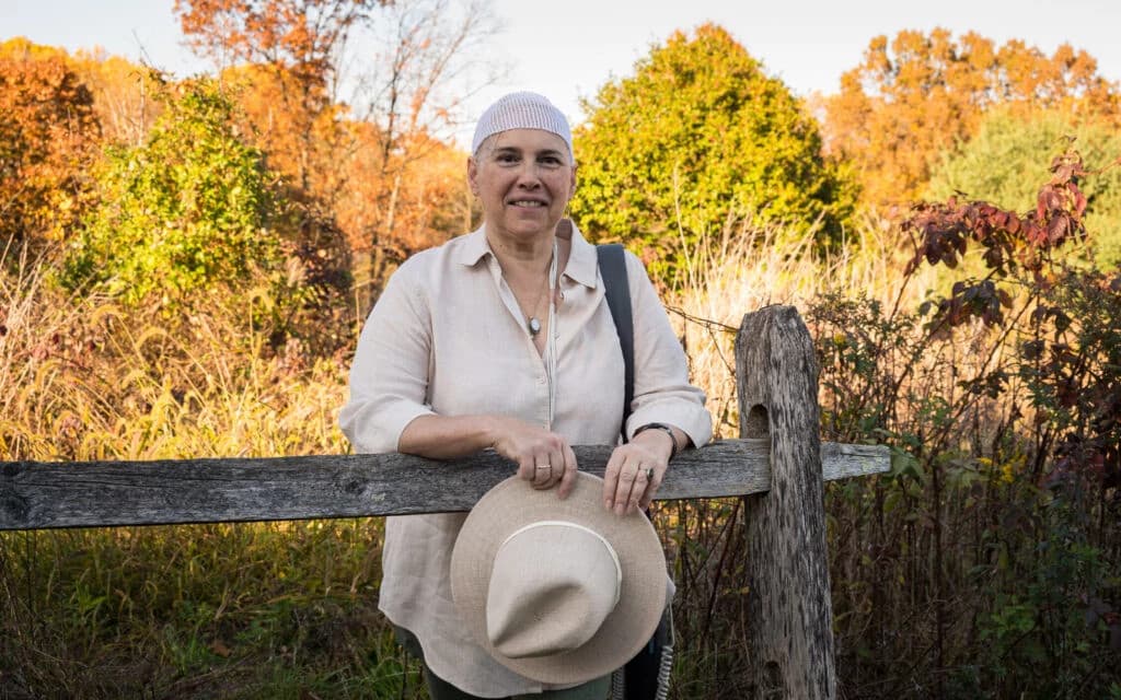 Portrait of smiling woman with black curly hair wearing a hat and gray sweater outdoors
